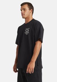 Black cotton t-shirt with a crew neckline and short sleeves. Features white printed text and graphic on the chest. Relaxed fit.