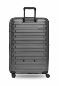 Valise rigide gris foncé avec des rainures horizontales, une poignée extensible, quatre roues rotatives et deux points de verrouillage sur le panneau avant.