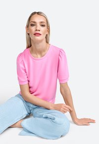 Top rosa a maniche corte con spalle a sbuffo, scollatura rotonda e texture liscia, abbinato a jeans a gamba larga blu chiaro.