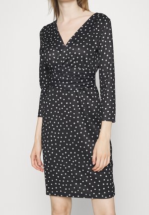 Schwarzes Pünktchenkleid mit langen Ärmeln und V-Ausschnitt, das eine taillierte Silhouette und geraffte Details an der Taille aufweist.