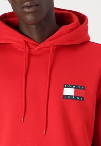 Felpa rossa con cappuccio e cordino, caratterizzata da una toppa rettangolare in blu navy, bianco e rosso. Realizzata in un morbido tessuto testurizzato.