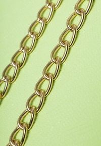 Cadenas de metal dorado sobre un fondo texturizado de color verde claro. Los eslabones tienen forma ovalada con un acabado brillante, entrelazándose en dos filas.