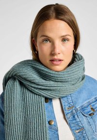 Jasnoniebieski, prążkowany szalik wykonany z miękkiego materiału, owinięty wokół szyi, w połączeniu z dżinsową kurtką z złotymi guzikami i detalami stębnowania.