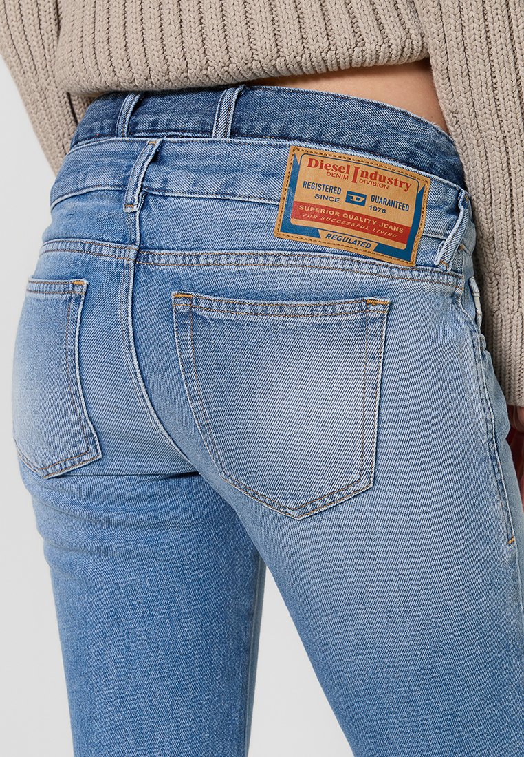 Jeans in denim blu con vita alta, caratterizzati da un'etichetta in pelle beige, design a cinque tasche e finitura sbiadita. La texture è liscia con lievi segni di usura.