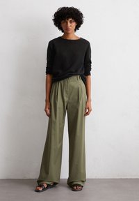 Schwarzer strukturierter Pullover mit rundem Ausschnitt, kombiniert mit olivgrünen Hosen mit hoher Taille und Falten sowie schwarzen Sandalen mit breiten Riemen.