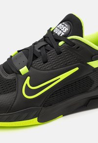 Crna atletska cipela s teksturiranim sintetičkim gornjištem, limeta zeleni naglasci i podstavljeni ovratnik. Ima istaknuti Nike swoosh i glatku sol.