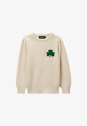 Pull en tricot couleur crème avec un col rond. Présente un patch en feutre vert en forme de trèfle sur la poitrine gauche. Manches et ourlet à côtes.