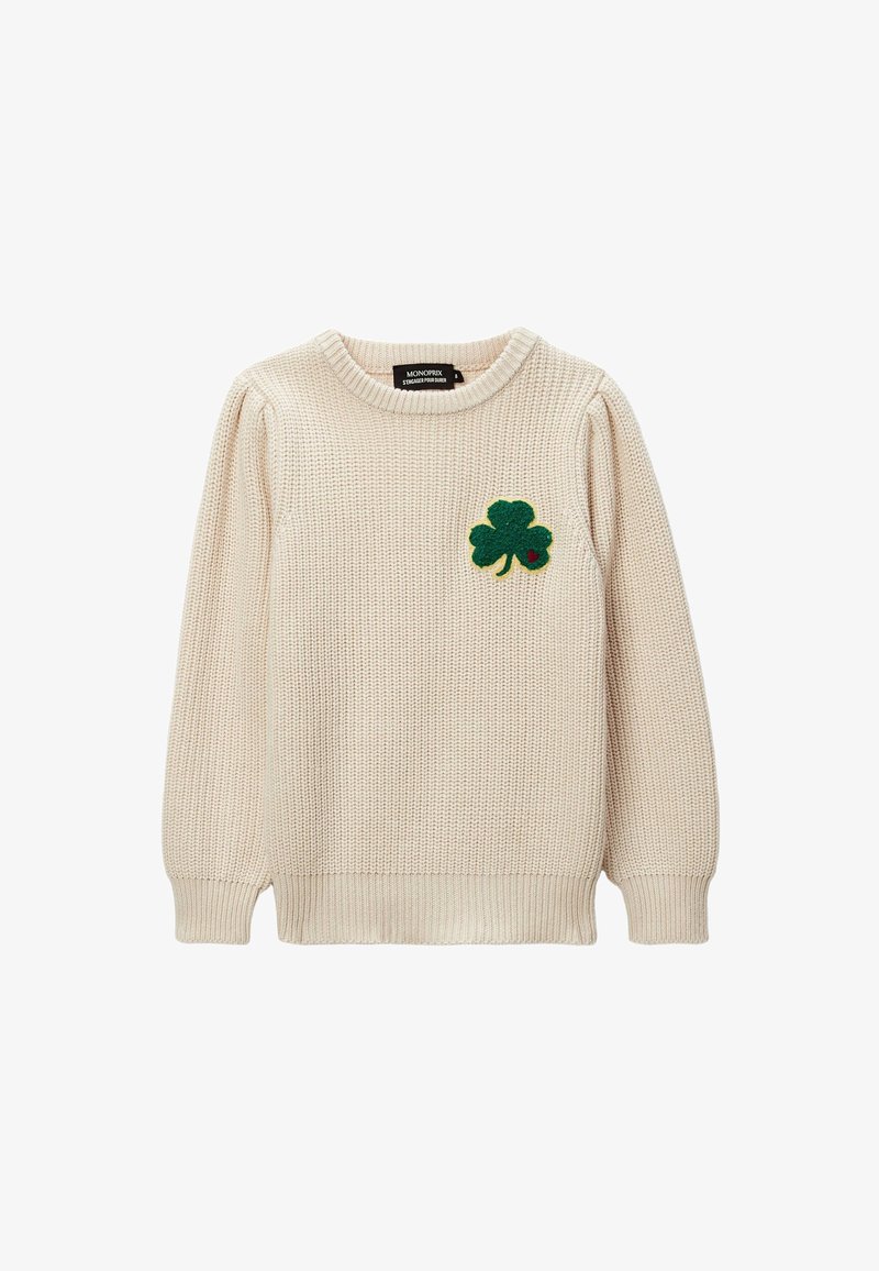 Pull en tricot couleur crème avec un col rond. Présente un patch en feutre vert en forme de trèfle sur la poitrine gauche. Manches et ourlet à côtes.
