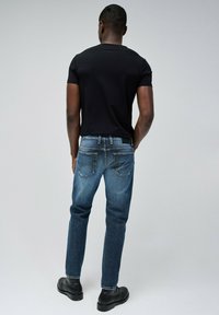 Camiseta oscura combinada con jeans de mezclilla azul de corte recto, cinco bolsillos y detalles de costura. Botas negras completan el look.