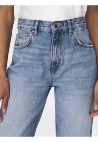 Jeans de tiro alto en azul claro con cierre de botón, cinco bolsillos y costuras de contraste. La tela presenta una textura suave y descolorida.