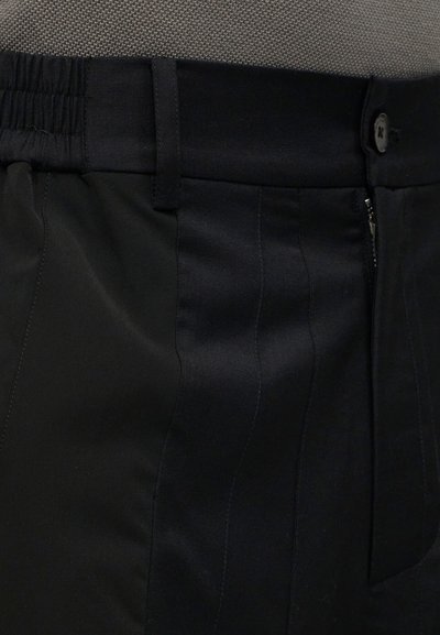 Μαύρο παντελόνι με ελαστική μέση και κούμπωμα με κουμπί, που δείχνει λεπτομερείς ραφές και υφή υφάσματος.