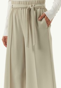 Lichte beige wijde broek met een zachte textuur, met een elastische tailleband en een gestrikt ceintuur. Zichtbare zijzakken.