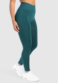 Leggings turquoise taille haute en tissu extensible ; texture lisse ; associés à des baskets de sport blanches ; sans motifs ni éléments métalliques visibles.
