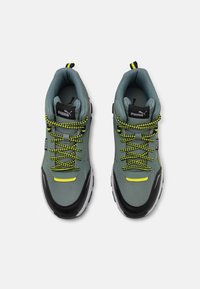 Puma sneakers feature a green upper, black accents, yellow detailing, and textured laces. They have a cushioned sole and ankle support.