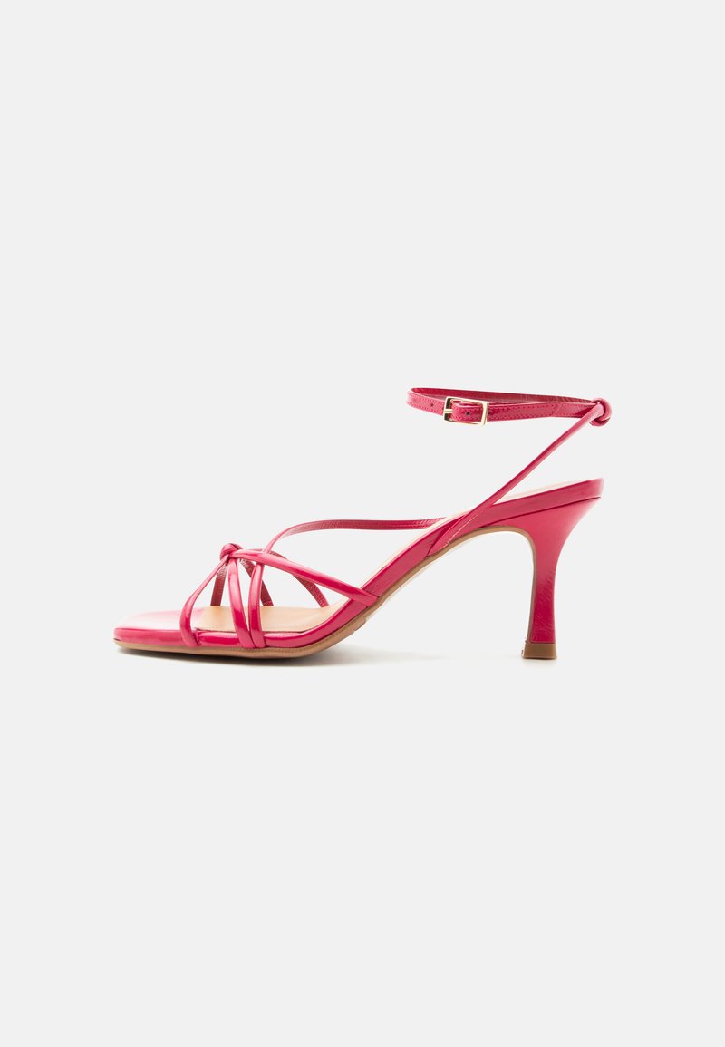 Sandale rose à talon haut avec brides, bout ouvert, fine bride à la cheville avec boucle et petit talon sur fond blanc uni.