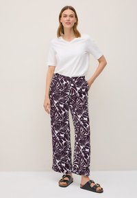 Hvid kortærmet V-udskåret t-shirt parret med brede lilla bukser med et hvidt bladmønster. Outfittet suppleres med sorte sandaler.