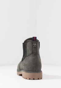 Šedá kotníková bota s poutkem, elastickými postranními panely a béžovou podrážkou s profilováním, z pohledu zespodu na bílém pozadí.