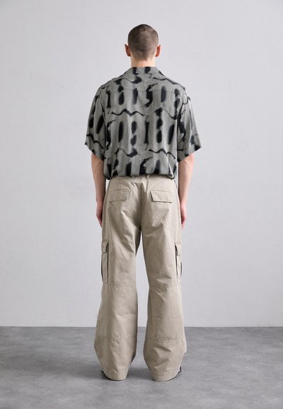 Chemise à manches courtes noire et blanche à motifs avec des rayures verticales, associée à un pantalon cargo beige avec poches latérales et une coupe décontractée.