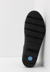 Black rubber shoe sole with textured grip patterns, embossed "HUNTER" logo, and a blue circular accent featuring a scale design.
