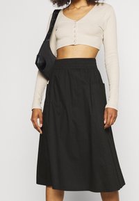 Falda negra de algodón con cinturilla elástica y bolsillos laterales, combinada con una blusa cortada de manga larga beige con botones.