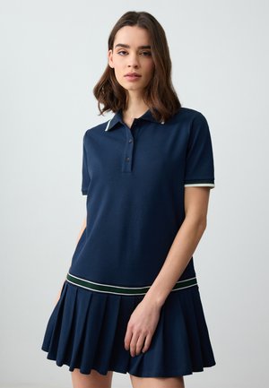 Marineblaues Polo-Kleid mit kurzen Ärmeln, mit einem Kragen, einer Drei-Knopf-Leiste und einem plissierten Rock mit grünen und weißen Streifen.