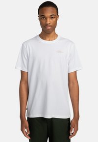 Hvid bomulds T-shirt med korte ærmer, rund halsudskæring og en subtil lys brun grafisk tekst på brystet. Stoffet virker glat og let.