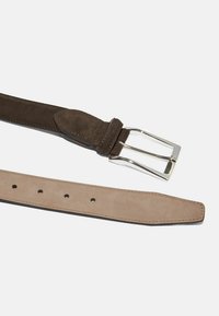 Cinturón de ante marrón con una hebilla de metal plateado. El cinturón tiene un extremo liso y afilado y múltiples agujeros para ajustes. Acabado con bordes cosidos.