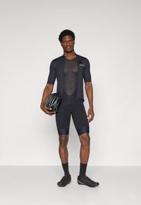 Maillot de vélo noir à manches courtes avec une couche intérieure en mesh, associé à un casque noir et des chaussures de cyclisme. Tissu lisse, coupe athlétique.