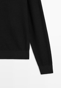 Pull noir à manches longues en tricot avec poignets et taille côtelés, présenté sur un fond blanc.