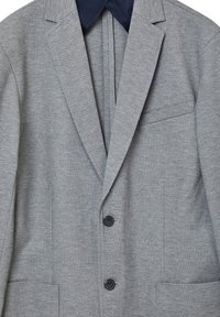 Blazer grigio a spina di pesce con colletto blu navy, due bottoni neri e tasca sul petto. Tessuto liscio con design su misura e spalle strutturate.
