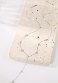 Collier en argent avec de petits accents étincelants. Présente un design délicat et des tailles de maillons variées, posé sur une surface en pierre texturée.