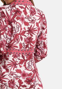 Rode bloempatron blouse met een witte basis, voorzien van lange mouwen, een kraag en textuuraccenten langs de taille en schouders.