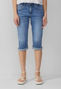 Jean capri bleu clair avec des ourlets roulés, style cinq poches et un léger délavage. Associés à des sandales à lanières crèmes.