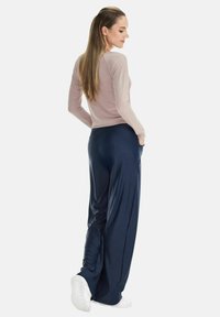 Long-sleeve light pink top and loose navy pants, made of smooth fabric. White sneakers complete the outfit; the model is facing away.
