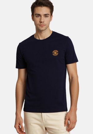 T-shirt blu navy in tessuto morbido, con un logo arancione circolare sul lato sinistro del petto e colletto girocollo classico.