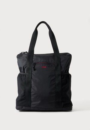 Sac cabas en nylon noir avec deux longues anses, poche avant zippée, poches latérales élastiques et petit logo rouge "HUGO" sur la poche avant.