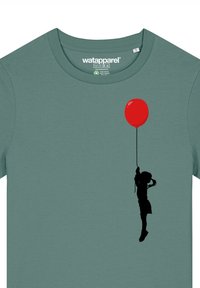 Groene katoen t-shirt met een zwarte silhouet van een kind dat een rode ballon vasthoudt, met een ronde halslijn en korte mouwen.