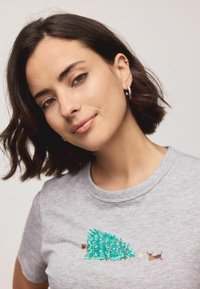 Šedé tričko s krátkym rukávom, na prednej strane vyšívaný kreslený vianočný stromček s ozdobami a hnedý pes v čiapke Santa.