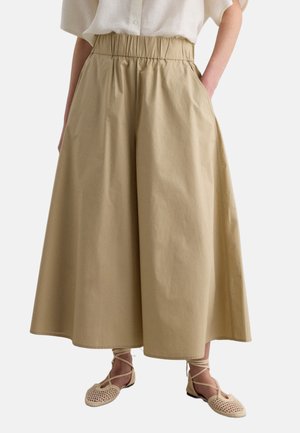 Pantalones beige de pierna ancha y corte cropped con cintura elástica, combinados con un top blanco roto con botones y zapatos planos beige tejidos con cordones.