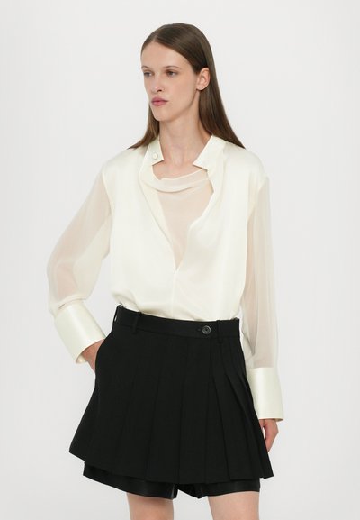 White sheer blouse with long sleeves and a tailored collar, paired with a high-waisted black pleated mini skirt.
