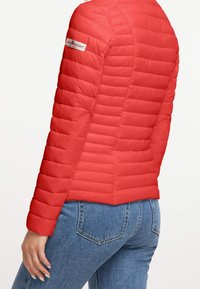 Chaqueta acolchada roja con diseño de cuadros horizontales, material liviano, puños elásticos y bolsillos laterales. Logo en el hombro izquierdo.