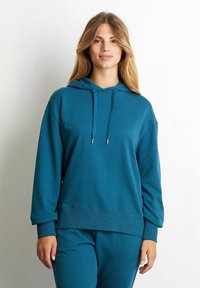 Felpa teal realizzata in tessuto morbido con una vestibilità rilassata, cappuccio con cordino e polsini e orlo a coste. Abbinata a pantaloni da tuta coordinati.