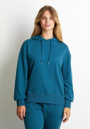 Teal hoodie van zacht materiaal met een ontspannen pasvorm, een capuchon met trekkoord en ribben aan de mouwen en onderkant. Gecombineerd met bijpassende sweatpants.