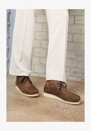 Brown leather shoes with laces, a rounded toe, and cream-colored rubber soles. The leather features a slightly worn texture.