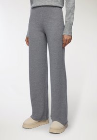 Pantaloni a gamba larga grigi a coste indossati con scarpe beige slip-on e un top grigio a maniche lunghe abbinato, mostrato dalla vita ai piedi.