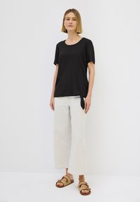 Schwarzes kurzärmliges Oberteil mit rundem Ausschnitt und seitlichem Bindedetail, kombiniert mit cremefarbenen weitgeschnittenen Hosen und braunen Riemchensandalen.