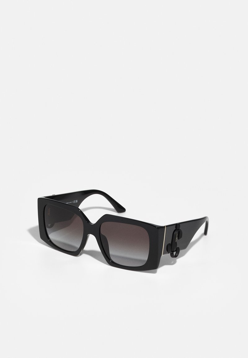 Lunettes de soleil noires rectangulaires avec des verres dégradés. La monture en plastique épaisse présente une courbe unique en haut et un accent logo distinct sur le côté.