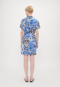 Vestido de manga curta com um tecido estampado floral em azul, preto e bege, com uma cintura ajustada e comprimento até ao joelho, e gola.