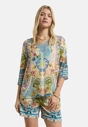 Woman wearing a loose-fitting, colorful floral and geometric patterned top with matching shorts, standing against a plain background.