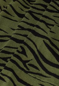 Tissu vert avec motif de rayures zèbre noires et texture tricotée visible, montrant des couches pliées.